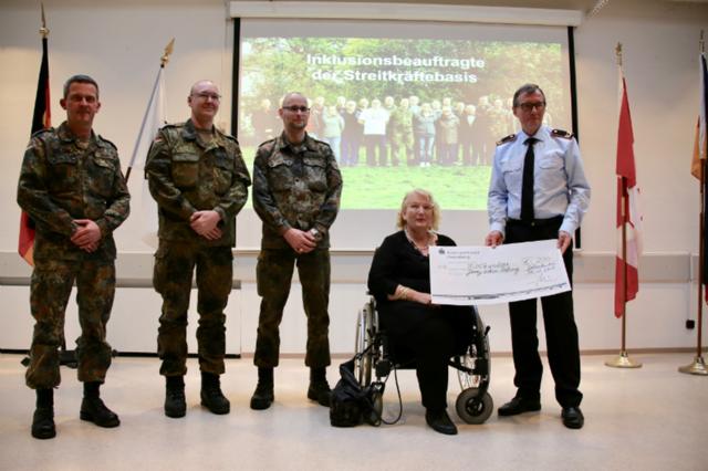 Eine Gruppe von Menschen mit einer Rollstuhlfahrerin, die einen Spendenscheck in ihren Händen hält.